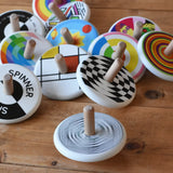 Bajo Modern Spinning Top spinning on a wooden surface with other wooden spinning top toys in the background. 