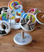 Bajo Modern Spinning Top spinning on a wooden surface with other wooden spinning top toys in the background. 