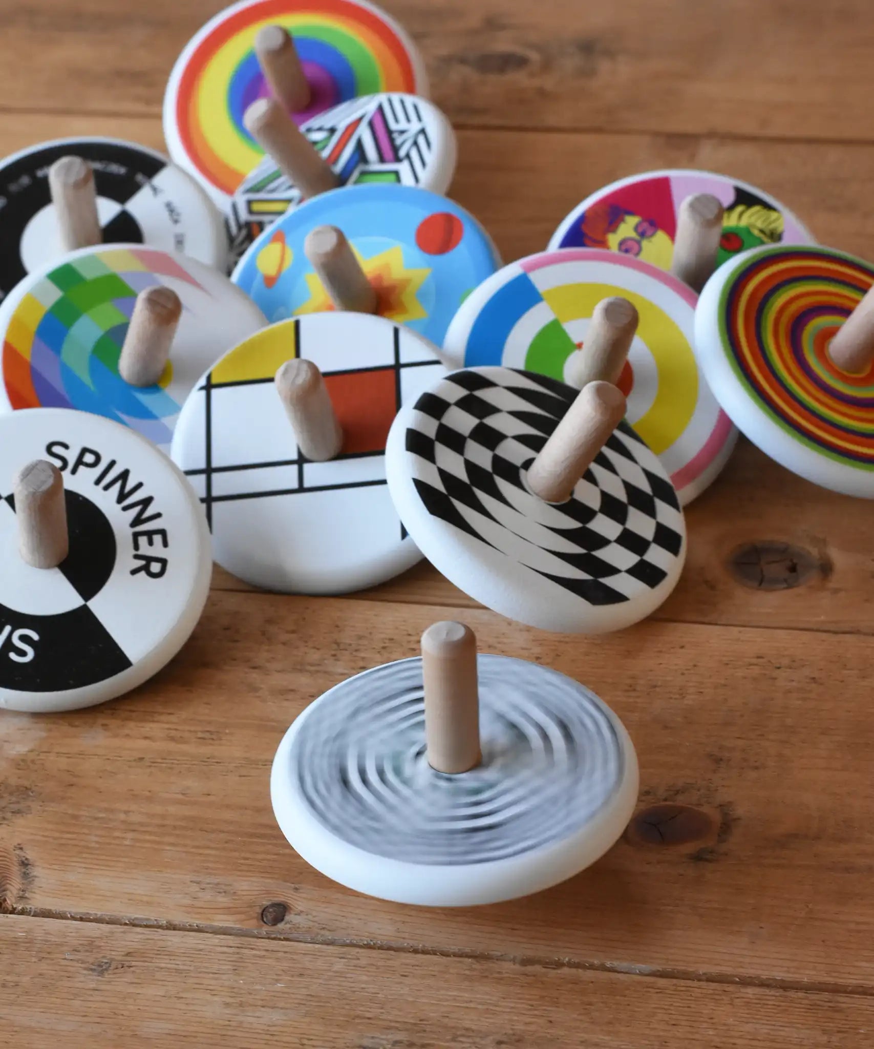 Bajo Modern Spinning Top spinning on a wooden surface with other wooden spinning top toys in the background. 