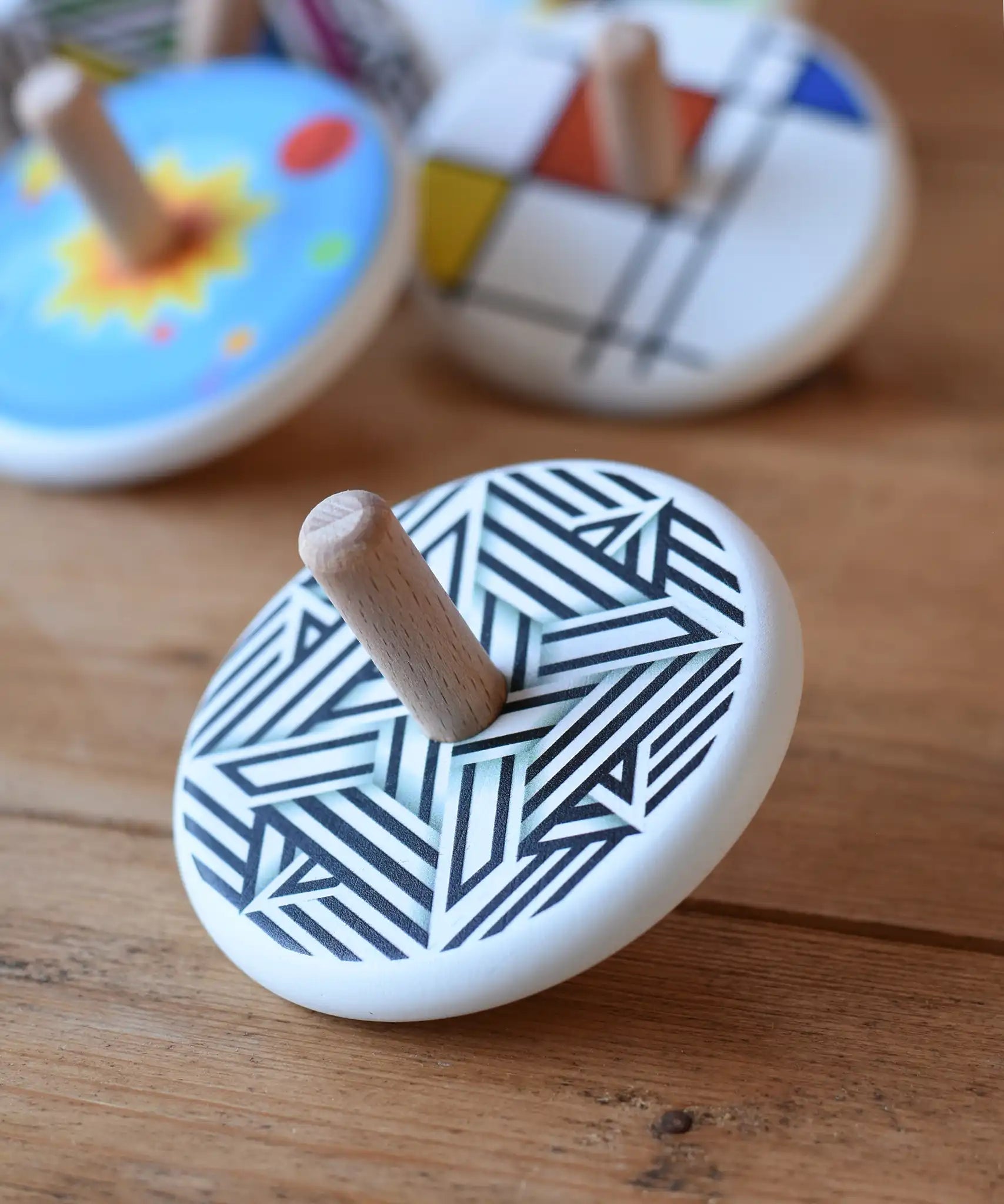 Bajo Modern Spinning Top placed on a wooden surface with other wooden spinning top toys in the background. 