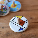Bajo Mondrian Spinning Top placed on a wooden surface with other wooden spinning tops in the background.