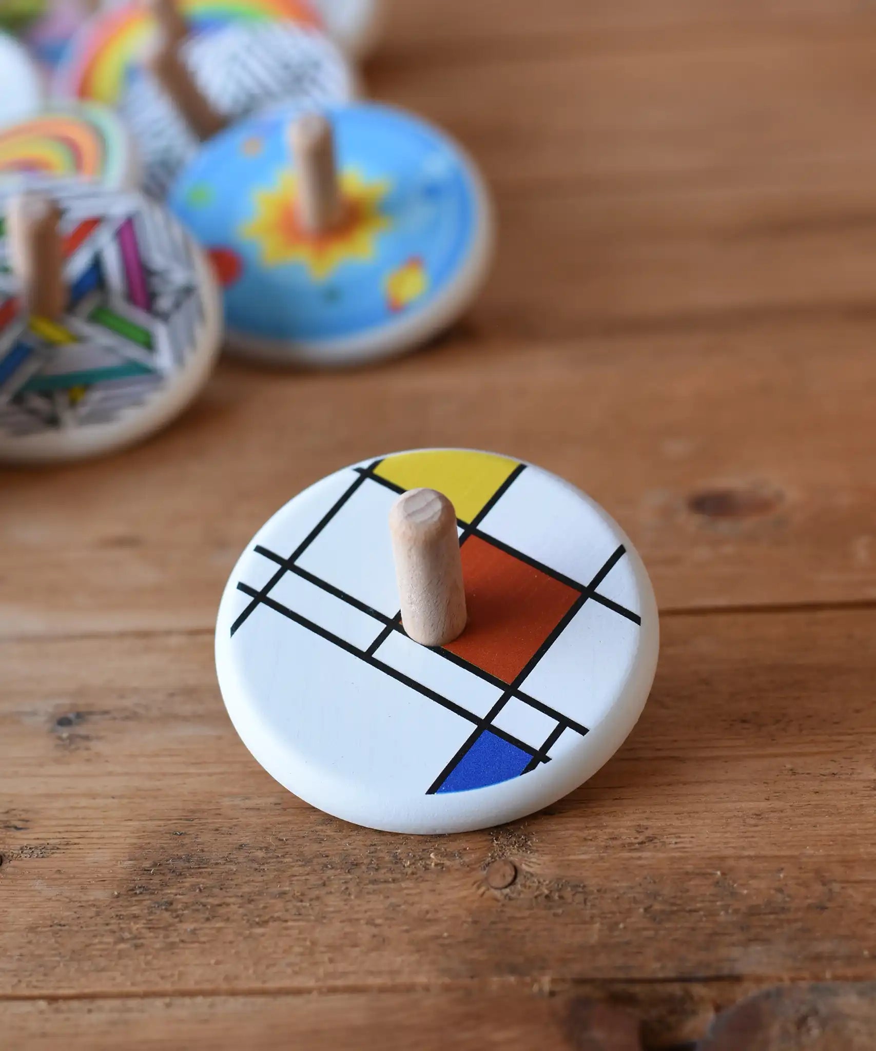 Bajo Mondrian Spinning Top placed on a wooden surface with other wooden spinning tops in the background.