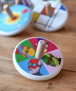 Bajo Pop Art Mr Bajor Spinning Top placed on a wooden surface with other wooden spinning tops in the background. 