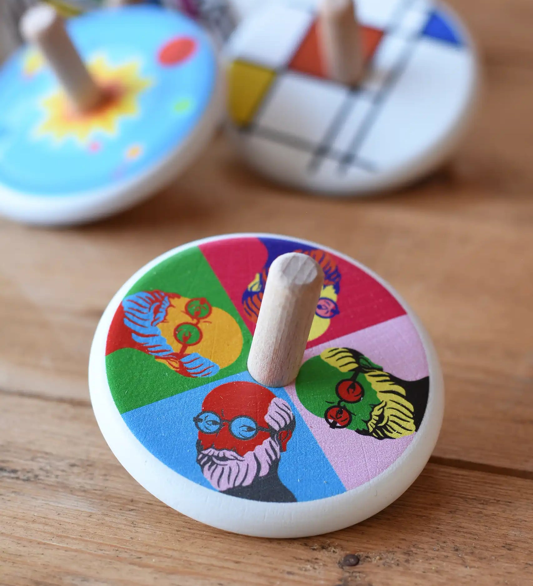 Bajo Pop Art Mr Bajor Spinning Top placed on a wooden surface with other wooden spinning tops in the background. 
