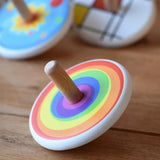 Bajo Rainbow Spinning Top placed on a wooden surface with other wooden spinning tops in the background. 