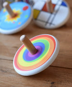 Bajo Rainbow Spinning Top placed on a wooden surface with other wooden spinning tops in the background. 
