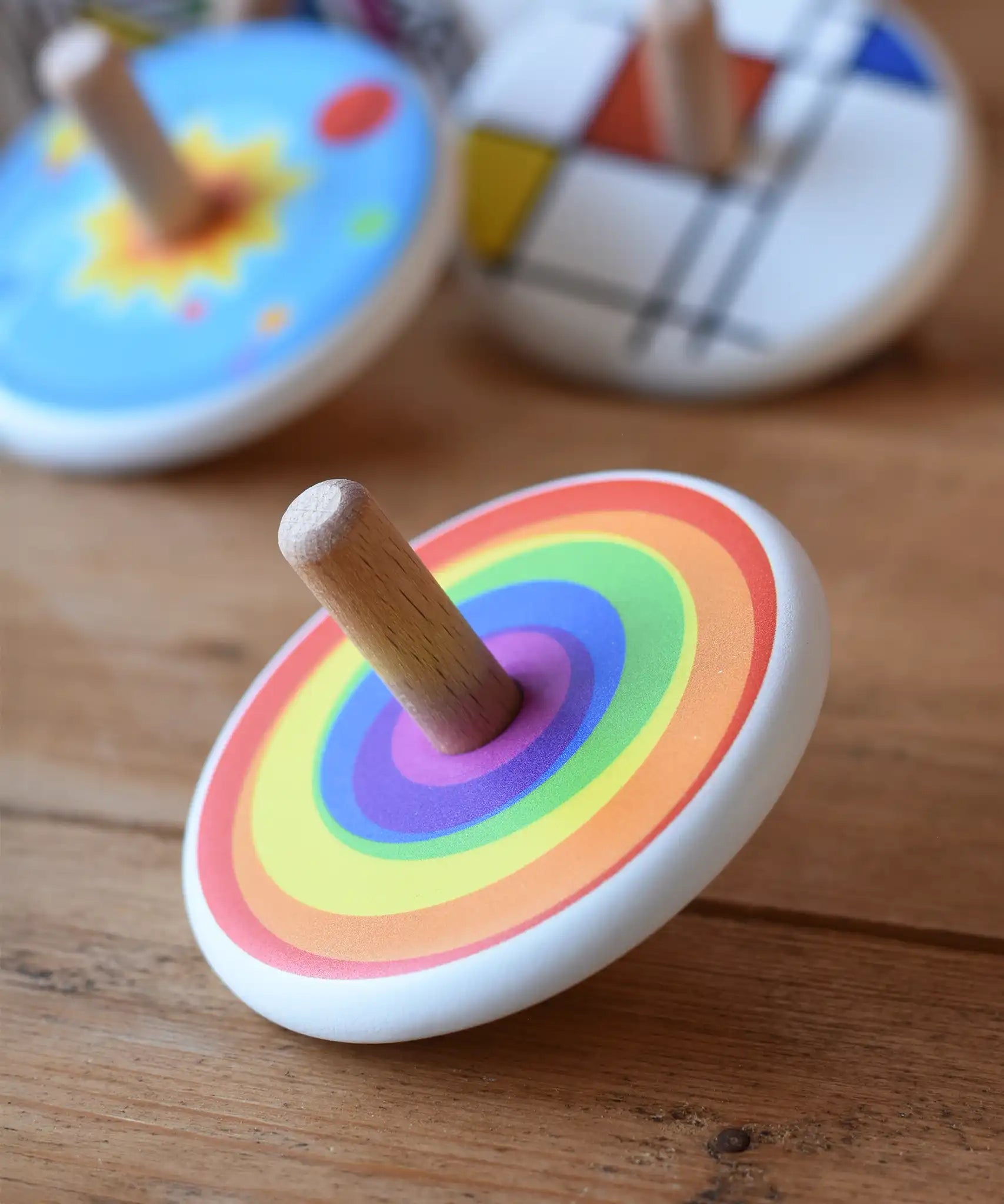 Bajo Rainbow Spinning Top placed on a wooden surface with other wooden spinning tops in the background. 