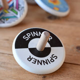 Bajo Black and White Spinning Top placed on a wooden surface with other Bajo wooden spinning top toys in the background.