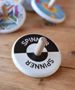 Bajo Black and White Spinning Top placed on a wooden surface with other Bajo wooden spinning top toys in the background.