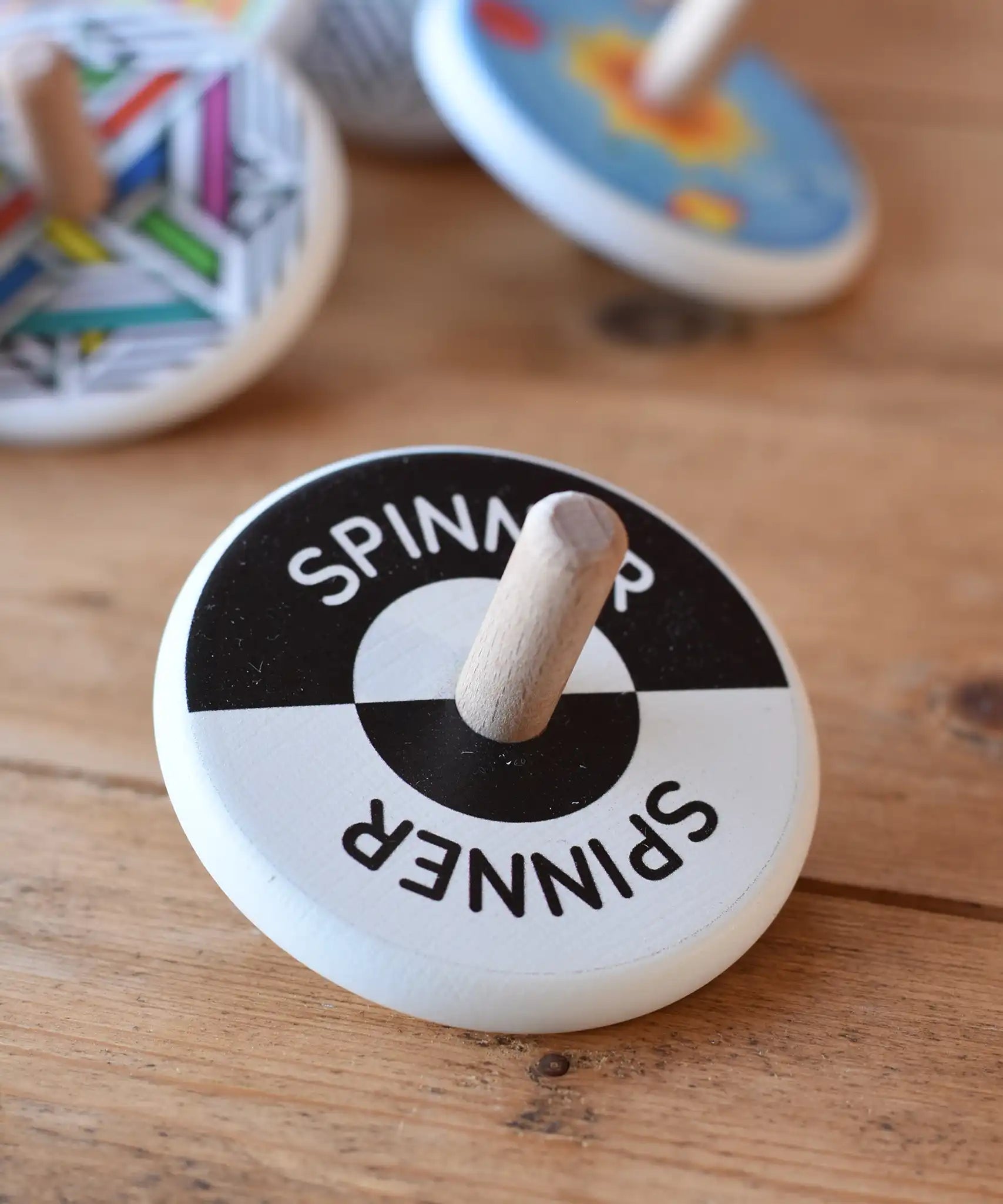 Bajo Black and White Spinning Top placed on a wooden surface with other Bajo wooden spinning top toys in the background.