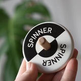 Bajo Black and White Spinning Top in an adult's hand showing the design on the top.