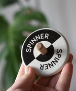 Bajo Black and White Spinning Top in an adult's hand showing the design on the top.