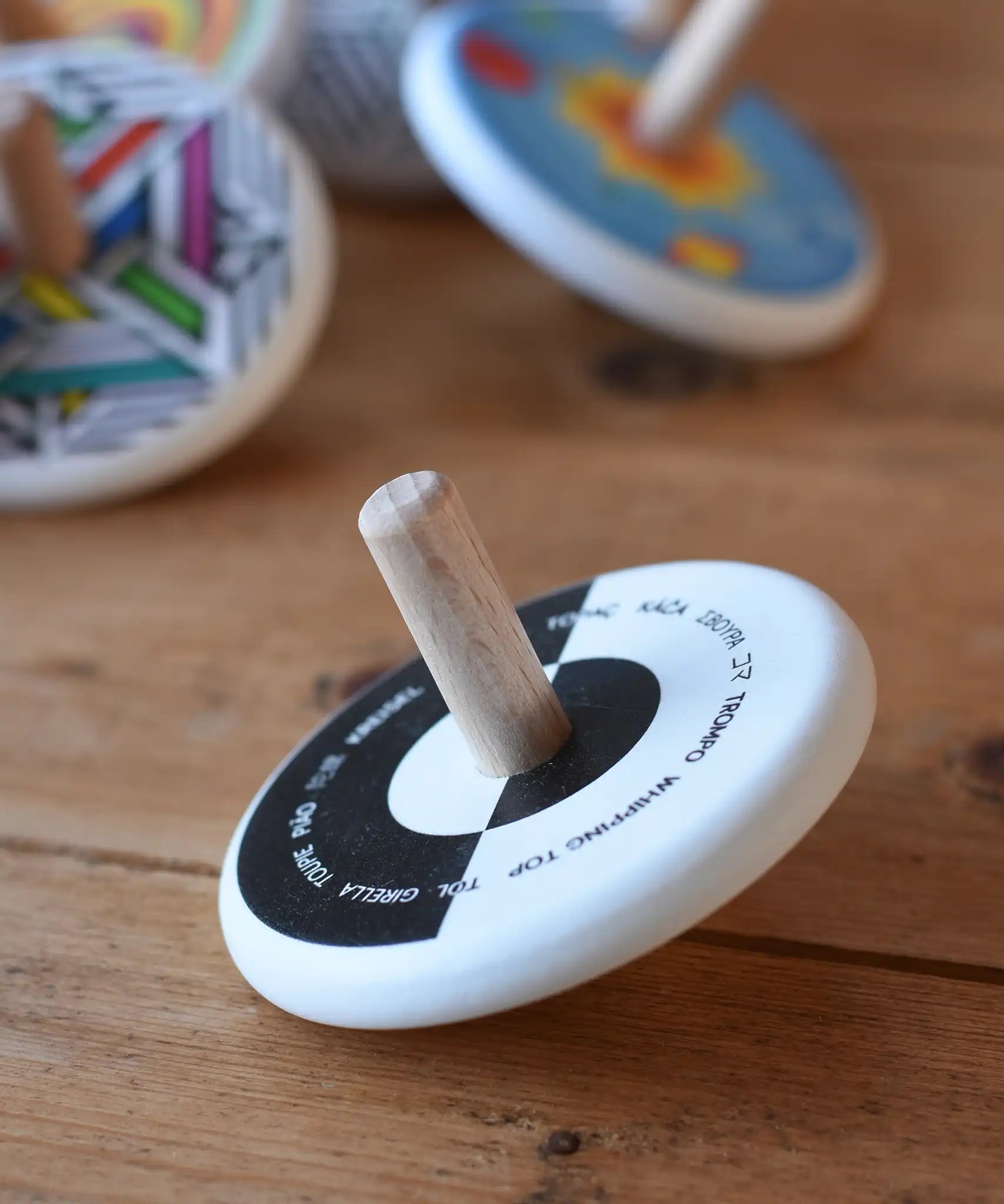 Bajo Languages Spinning Top placed on a wooden surface with other Bajo spinning top s in the background. 