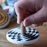 A close up of a child's hand spinning the Bajo Latern Spinning Top on a wooden surface.
