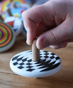 A close up of a child's hand spinning the Bajo Latern Spinning Top on a wooden surface.