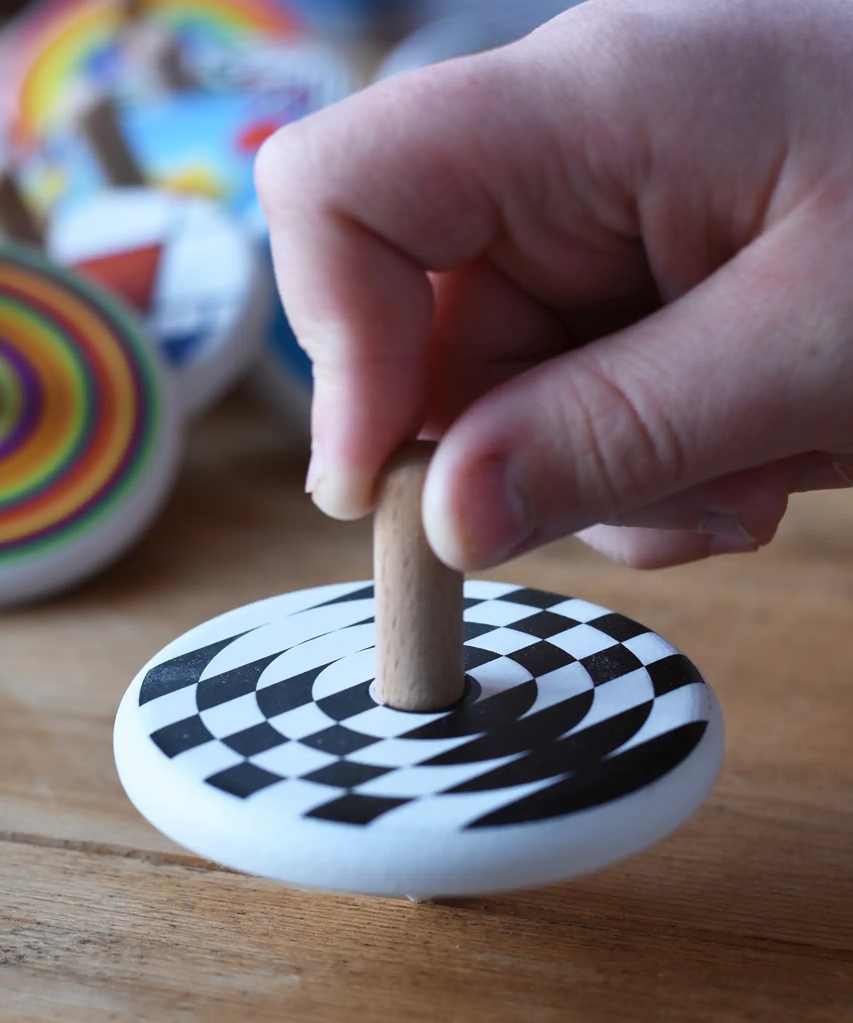 A close up of a child's hand spinning the Bajo Latern Spinning Top on a wooden surface.