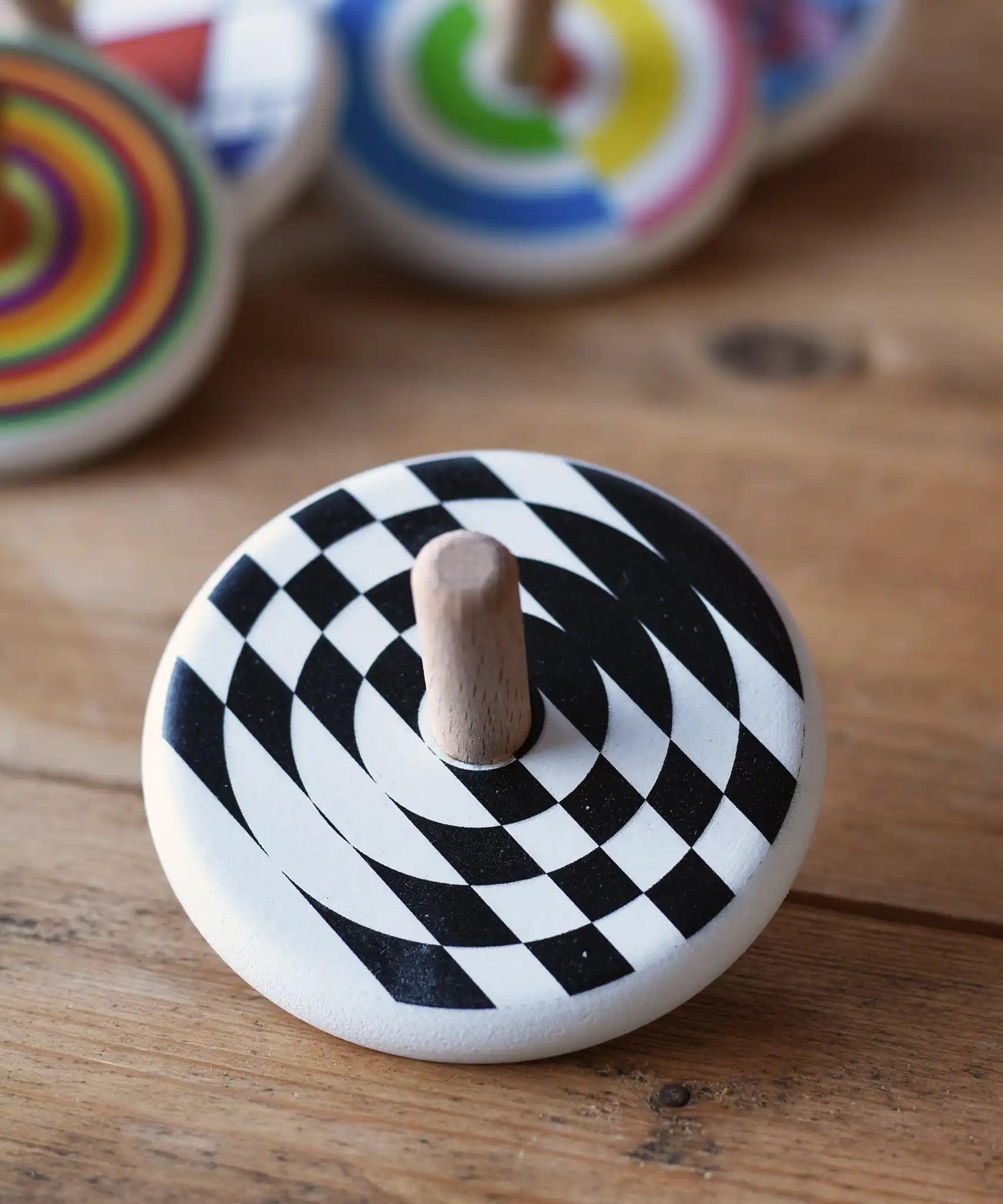 Bajo Latern Spinning Top placed on a wooden surface with other wooden spinning tops in the background.