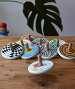 Bajo Mondrian Spinning Top spinning and blurred in motion a wooden surface with lots of other Bajo spinning tops placed in the background.