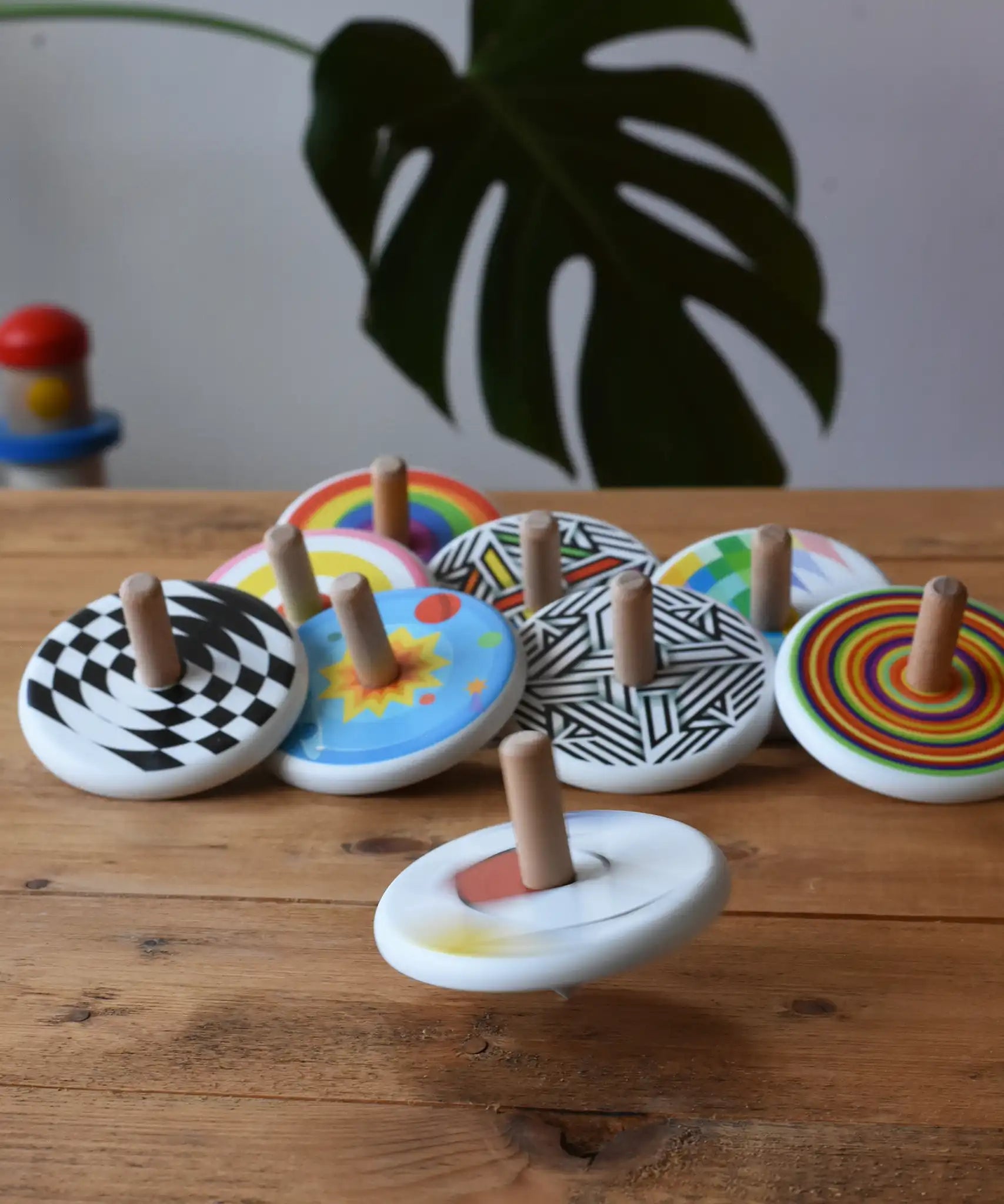 Bajo Mondrian Spinning Top spinning and blurred in motion a wooden surface with lots of other Bajo spinning tops placed in the background.