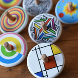 Bajo Mondrian Spinning Top placed on a wooden surface with lots of other colourful Bajo wooden spinning tops placed behind it.