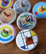 Bajo Mondrian Spinning Top placed on a wooden surface with lots of other colourful Bajo wooden spinning tops placed behind it.