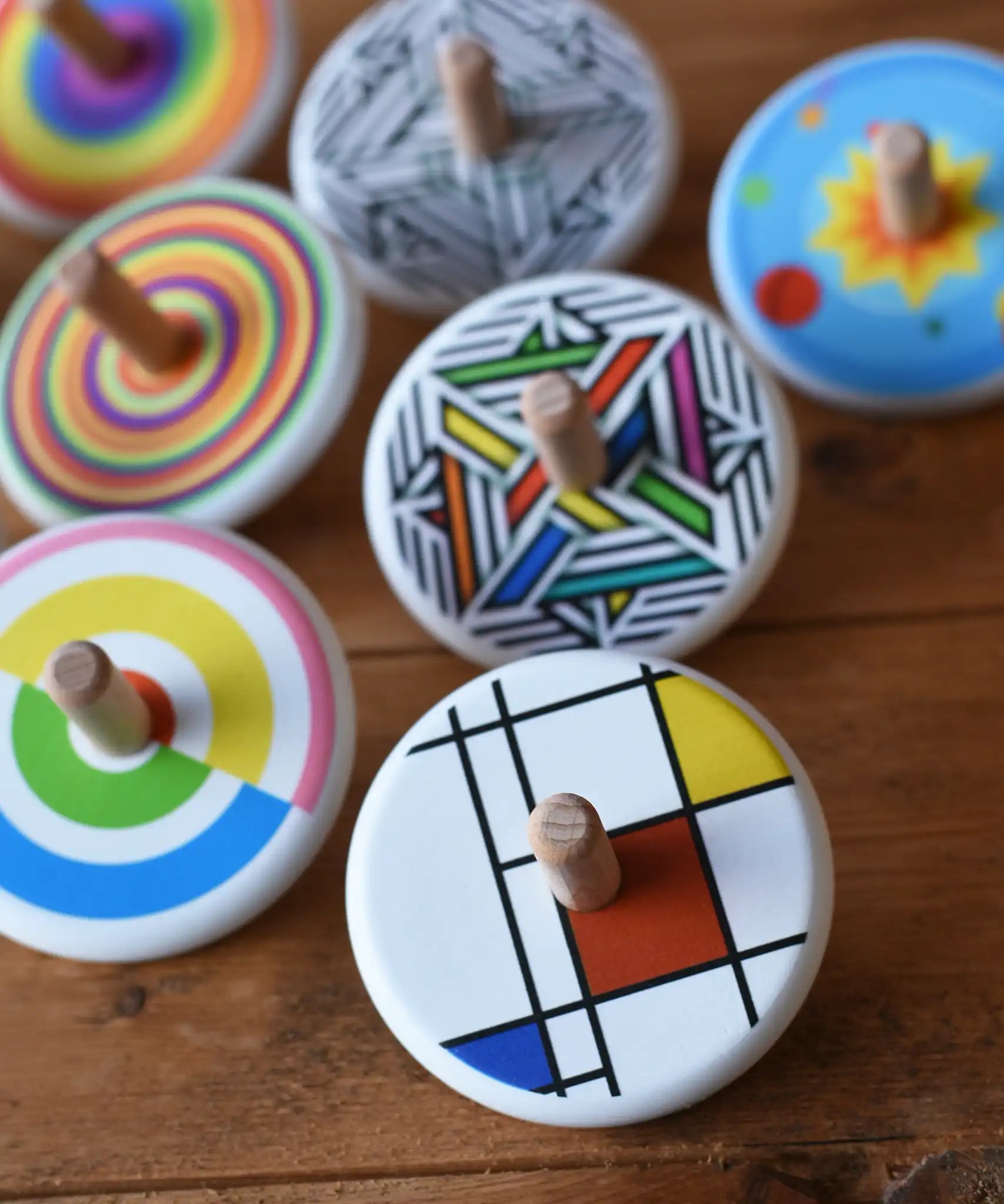 Bajo Mondrian Spinning Top placed on a wooden surface with lots of other colourful Bajo wooden spinning tops placed behind it.