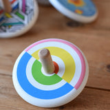 Bajo Colourful Semi Circles Spinning Top placed on a wooden surface with other wooden spinning top toys in the background.