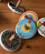 Bajo Universe Spinning Top placed on a wooden surface surrounded by other design of Bajo wooden spinning tops. 