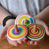 Three Bajo spinning tops in a child's hands each with a diffrent design, colourful semi circles, circles and rainbow. 
