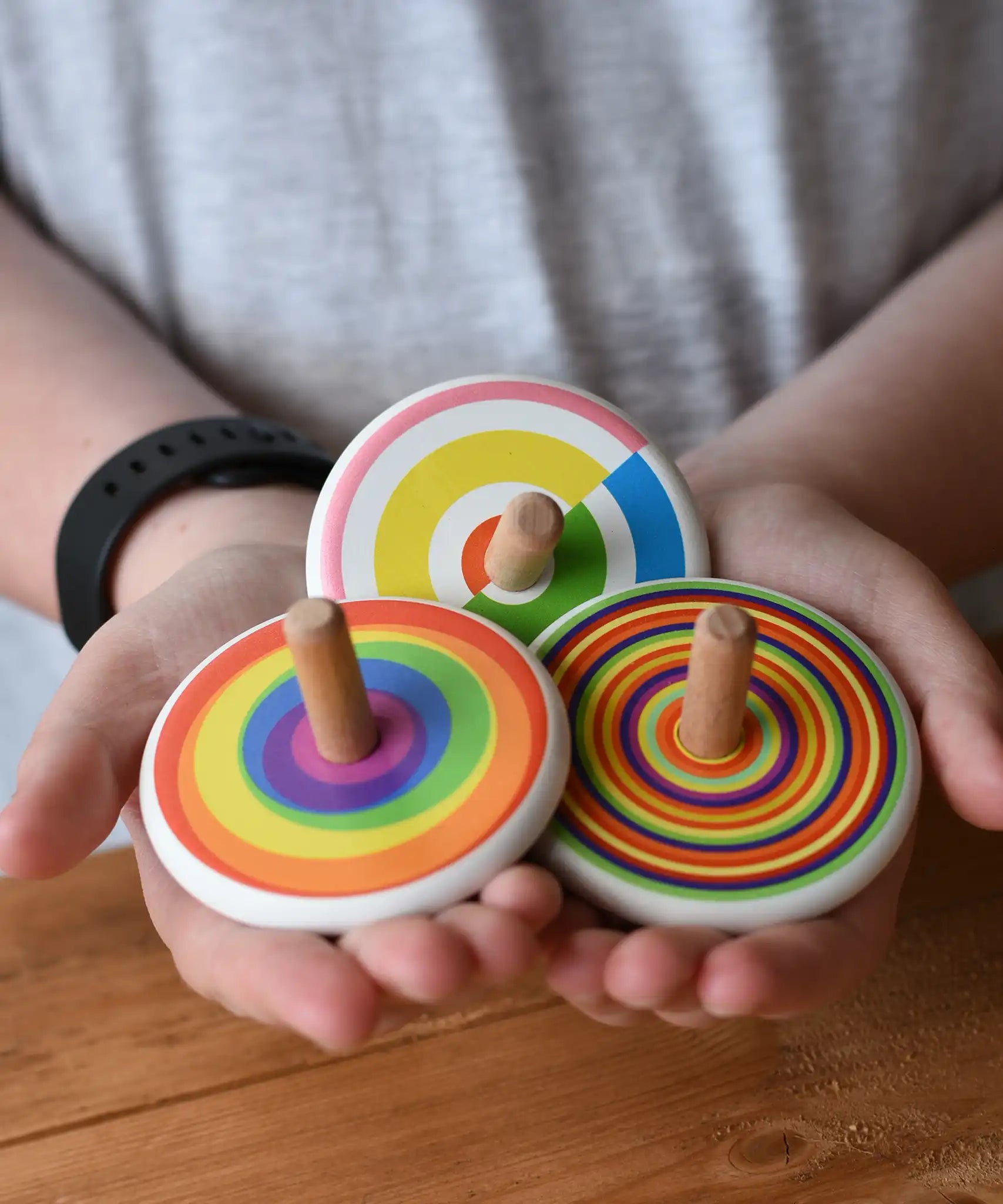 Three Bajo spinning tops in a child's hands each with a diffrent design, colourful semi circles, circles and rainbow. 