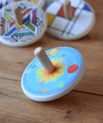 Bajo Universe Spinning Top placed on a wooden surface with other wooden spinning tops in the background.