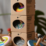 Three Bajo spinning tops in their cardboard packaging boxes tacked up with other Bajo spinning tops placed besides them.