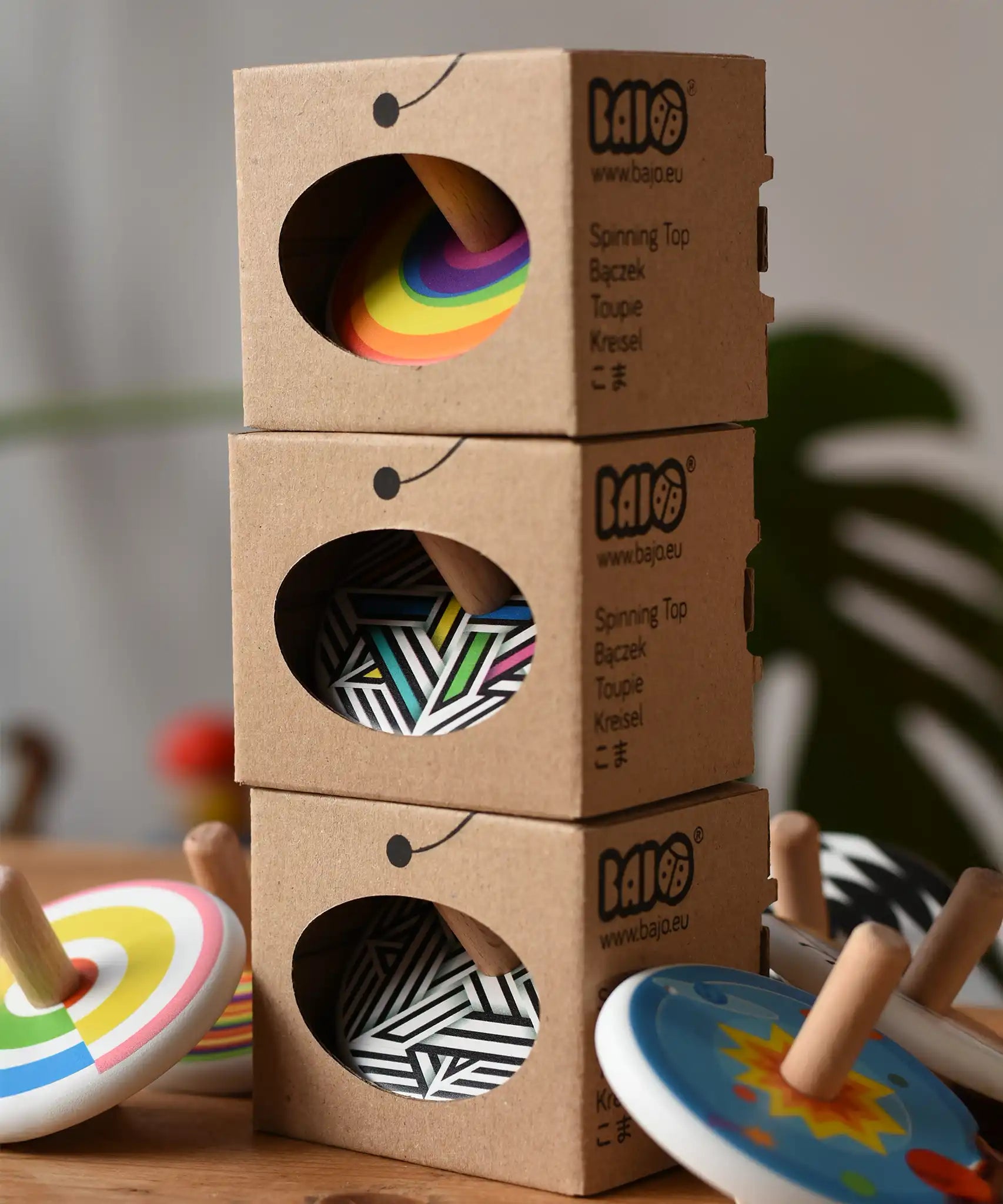 Three Bajo spinning tops in their cardboard packaging boxes tacked up with other Bajo spinning tops placed besides them.