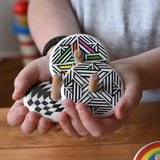 Three Bajo spinning tops in a child's hand each with a different design, latern design, modern and modern colour design tops.