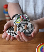Three Bajo spinning tops in a child's hand each with a different design, latern design, modern and modern colour design tops.