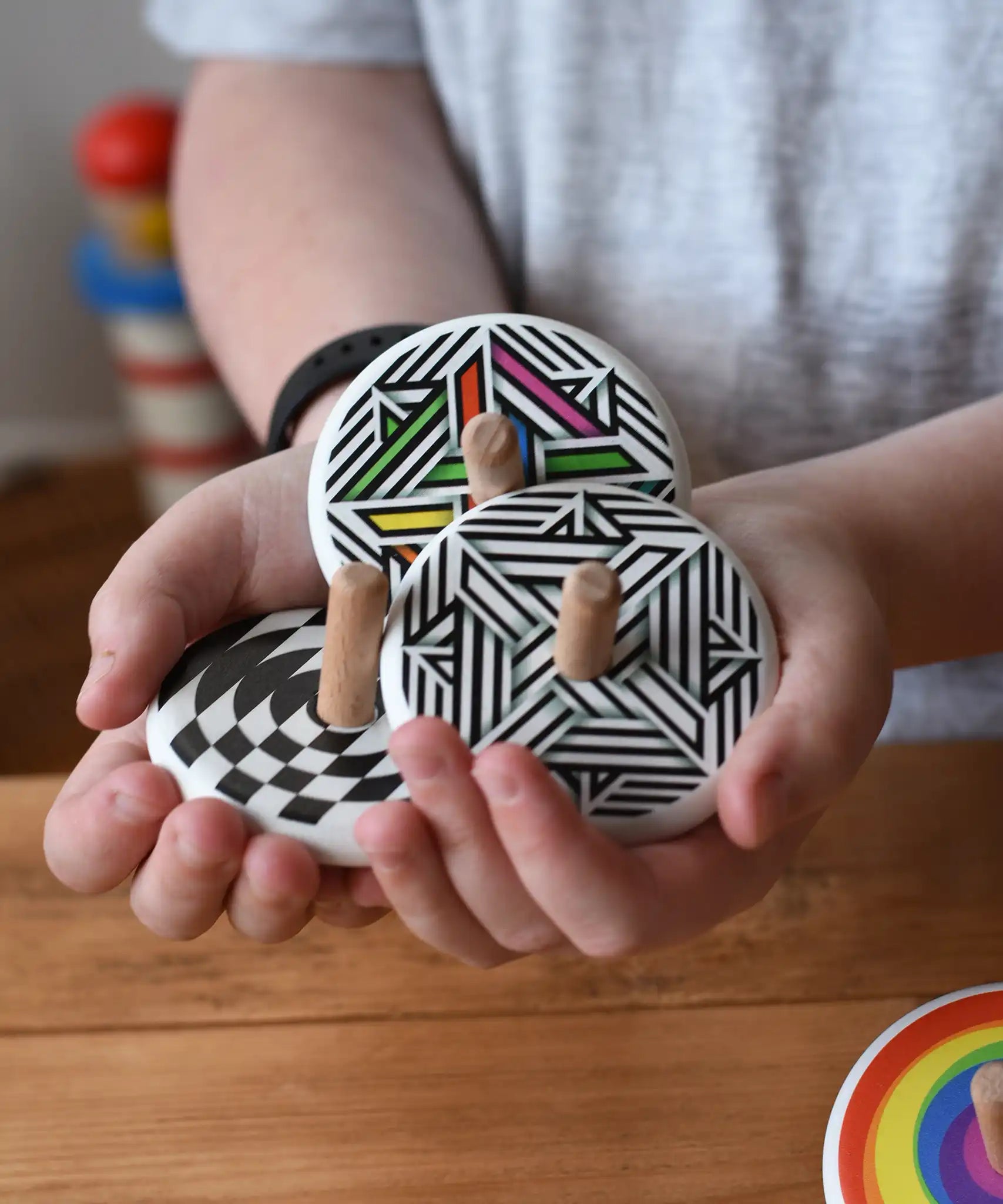 Three Bajo spinning tops in a child's hand each with a different design, latern design, modern and modern colour design tops.