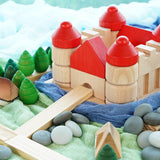 Bajo Castle Stacker toy on some green and blue fabric surrounded by Bumbu wooden houses and some Grapat mandala trees