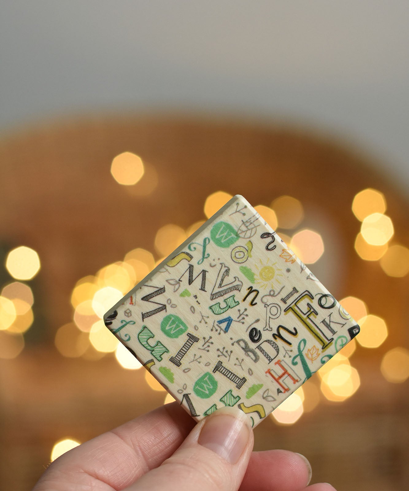 An adult holding up a tile from the Bajo Wooden Tiles Memory Game. The tiles have an illustration on one side and a mix of letters in different fonts on the other. These heirloom quality toys by Bajo are part of a wide range of wooden toys available here at Babipur.