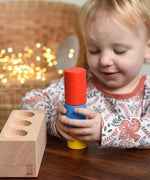 A child playing with the Bajo Deep And Shallow Sorter wooden toy placed on a small wooden table. The child is stacking the cylinder shaped blocks on top of each other. These heirloom quality toys by Bajo are part of a wide range of wooden toys available here at Babipur. 