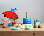 A selection of Bajo wooden toys placed on the Trimclimb Miri slide. A pull along dragon, rook tower stacker and a push along ghost. These wooden toys are part of a wide selection available at Babipur. 