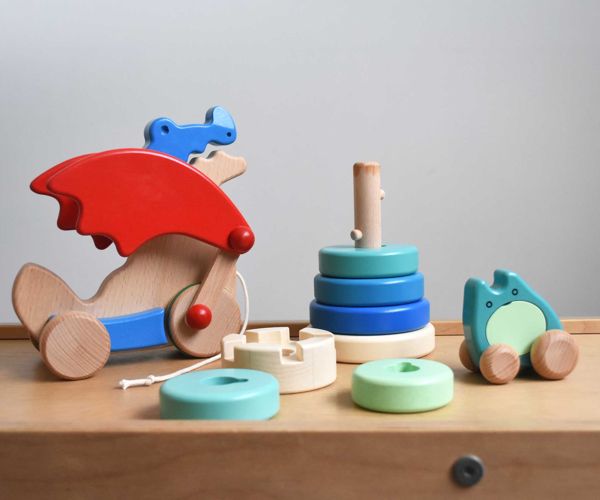 A selection of Bajo wooden toys placed on the Trimclimb Miri slide. A pull along dragon, rook tower stacker and a push along ghost. These wooden toys are part of a wide selection available at Babipur. 