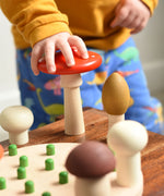 A close up of a child's hand grabbing the red fly agaric mushroom from the Bajo Wooden Mushroom Forest Peg Puzzle set. These heirloom quality toys by Bajo are part of a wide range of wooden toys available here at Babipur. 