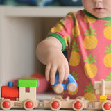 Child putting a blue car on top of the carriage from the Bajo wooden train o build set