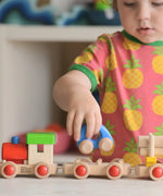 Child putting a blue car on top of the carriage from the Bajo wooden train o build set