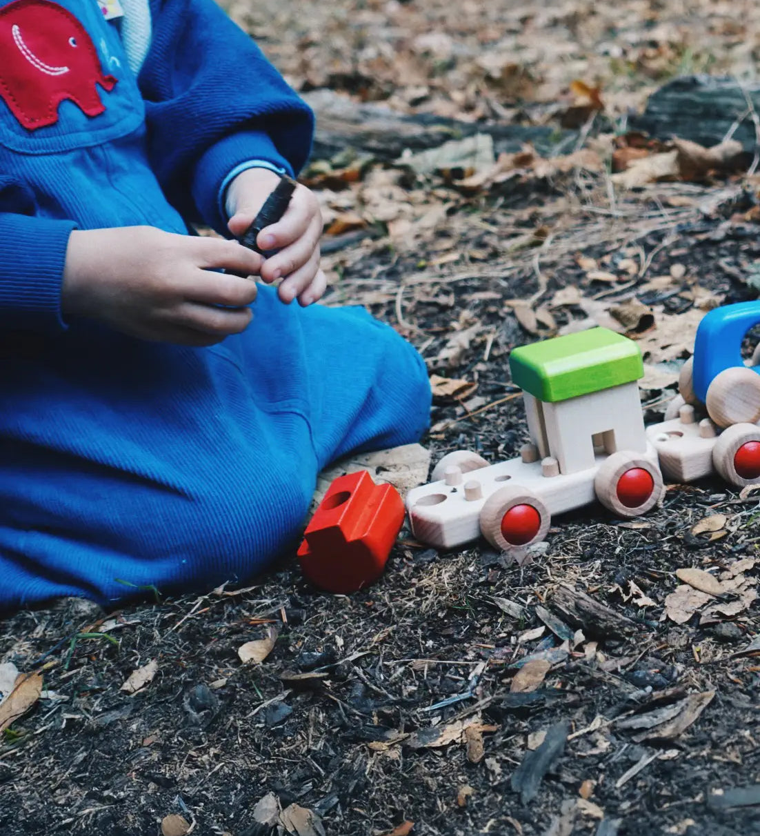 Child on the floor building a Bajo wooden train. 