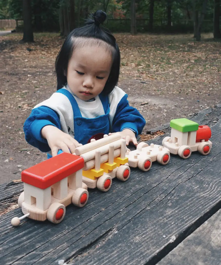 Child playing with the Bajo wooden train to build set on a table in the park 
