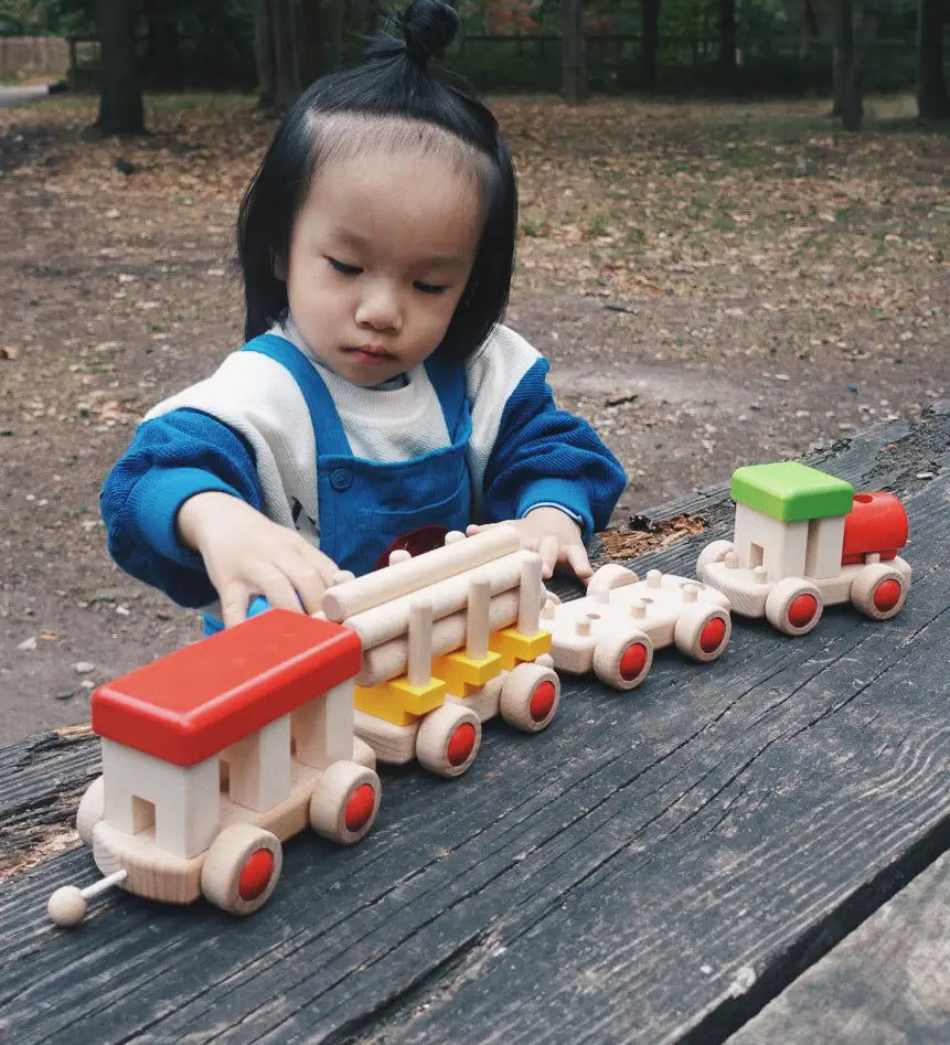 Child playing with the Bajo wooden train to build set on a table in the park 