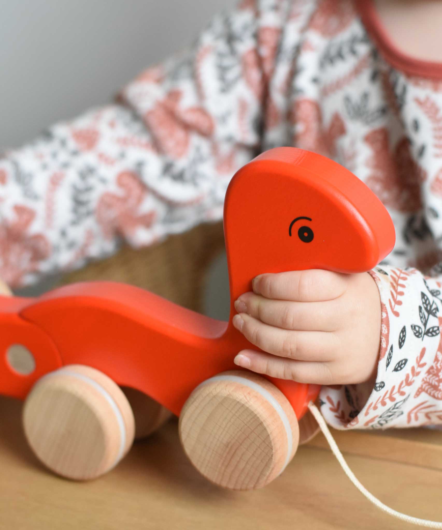 A close up of a child's hand holding a red coloured Bajo pull along worm toy. These heirloom quality toys by Bajo are part of a wide range of wooden toys available here at Babipur. 