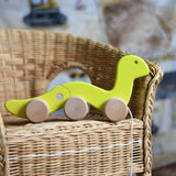 A green coloured Bajo wriggling worm pull along toy placed on a child's wicker chair. These heirloom quality toys by Bajo are part of a wide range of wooden toys available here at Babipur. 