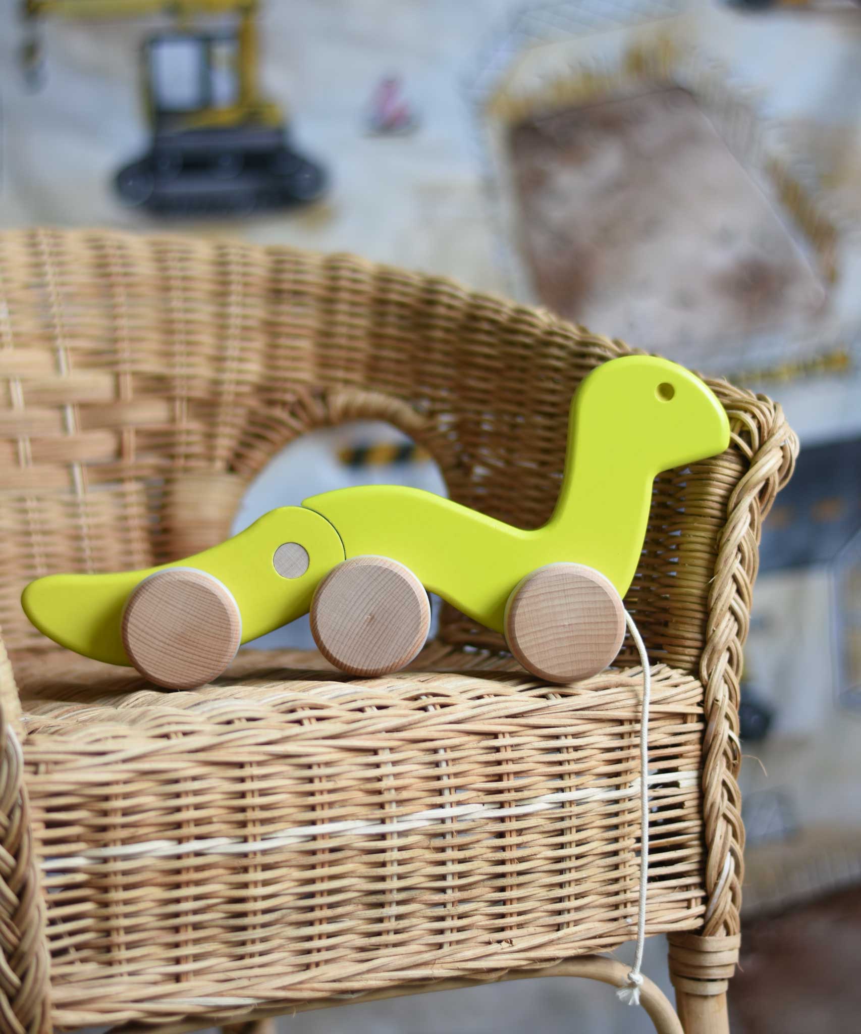 A green coloured Bajo wriggling worm pull along toy placed on a child's wicker chair. These heirloom quality toys by Bajo are part of a wide range of wooden toys available here at Babipur. 